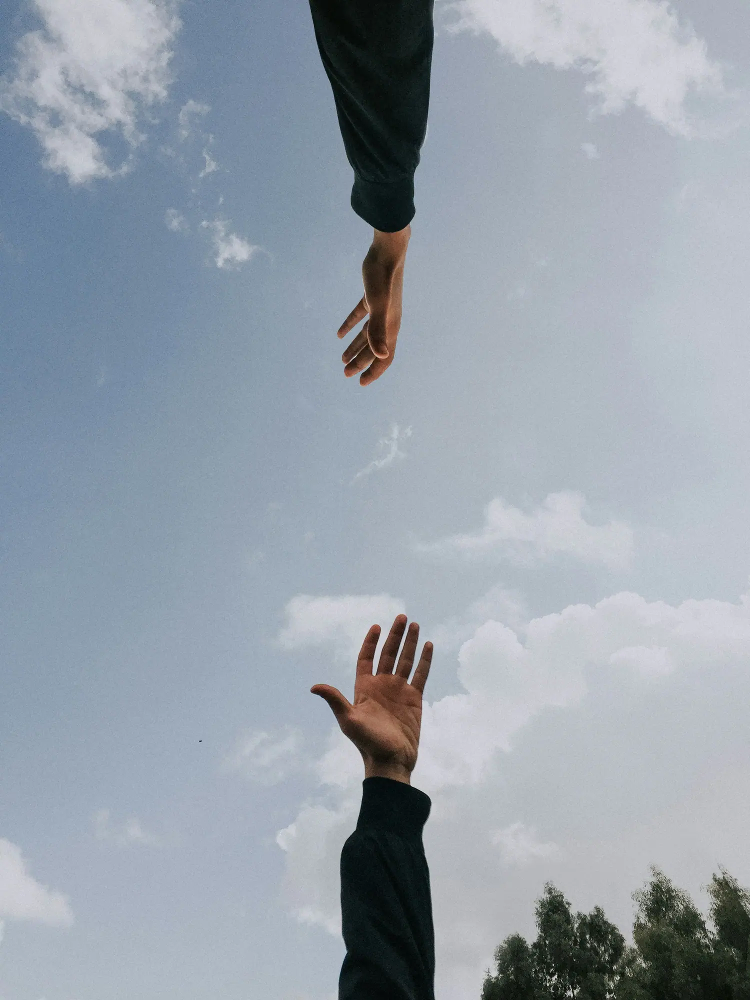 Two hands reaching toward each other against an open sky